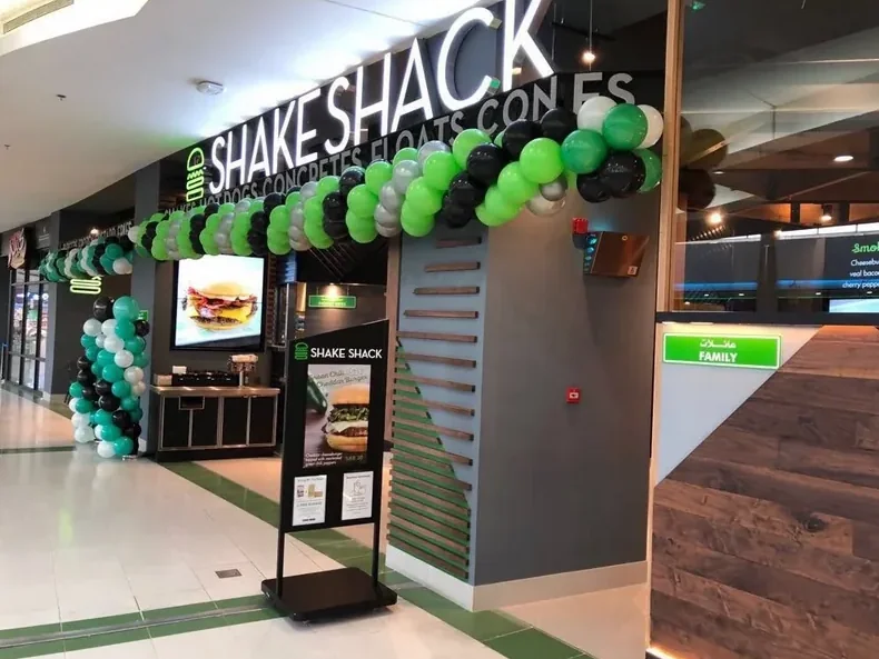 A completed Shake Shack storefront on opening day, a green and white balloon arch framing the slatted timber entry.
