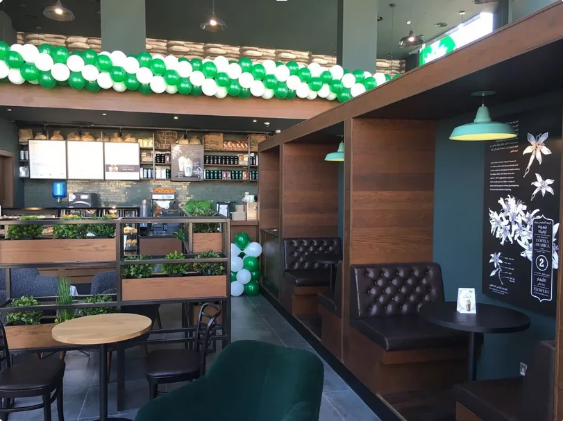 A completed Starbucks interior: the order counter and tiered merchandising shelves on the left, dark leather banquettes under pendant lighting on the right.