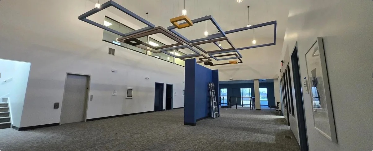 The 82nd St. Workspace lobby: a suspended rectilinear light sculpture over the elevator bank, with a navy accent column and grey carpet.